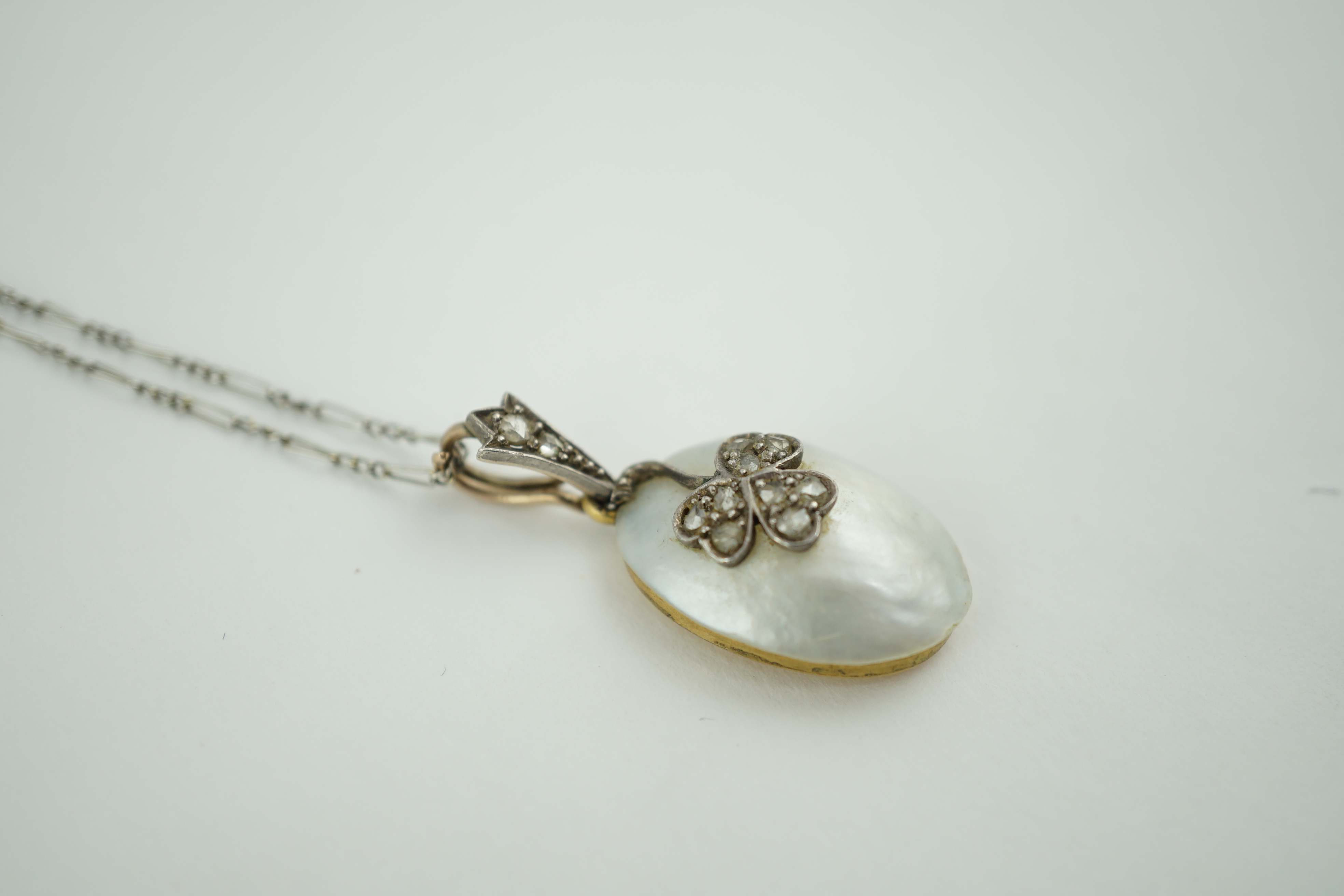 A 1920's gold and mabe pearl set oval pendant, with rose cut diamond set floral motif, on a platinum chain